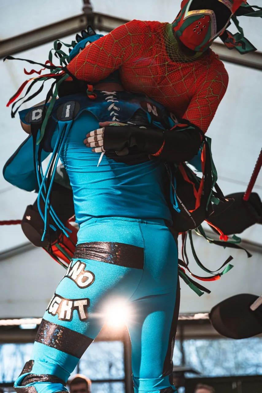 A wrestler in a costume having another wrestler on the shoulder.
